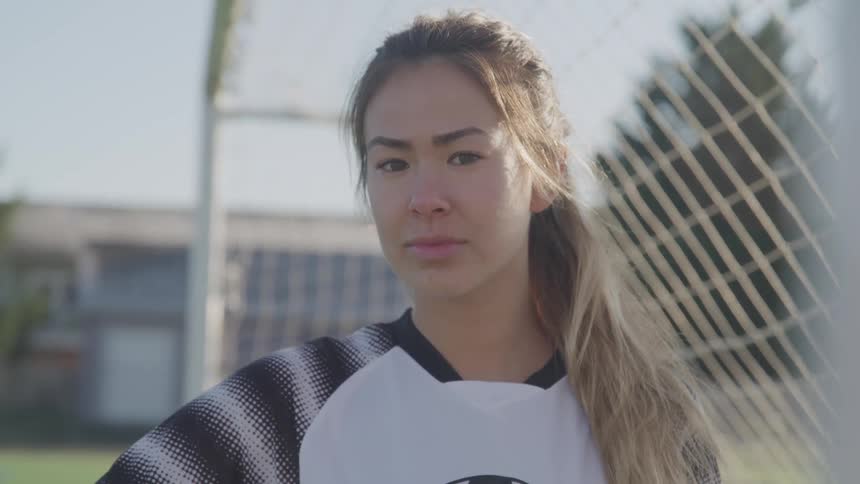 A teenage girl standing in a soccer net