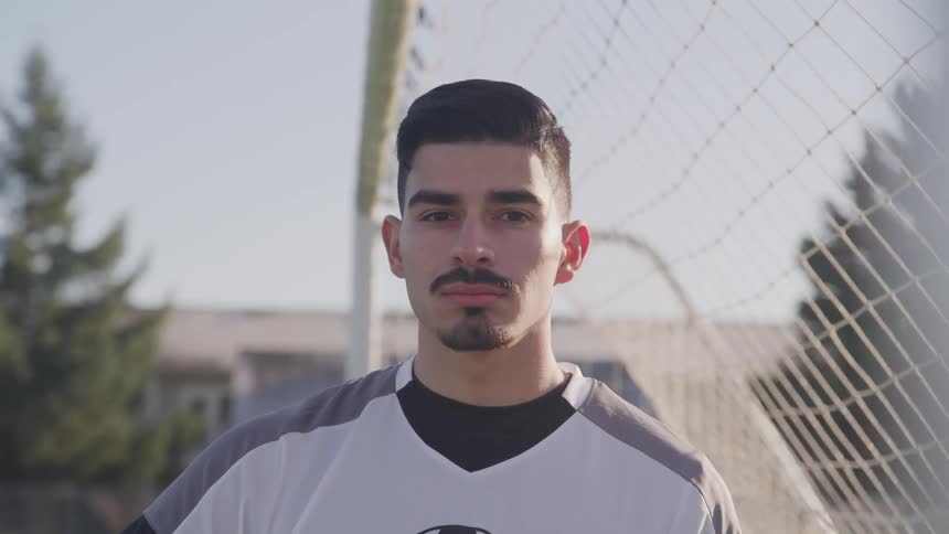 A teenage boy standing in a goalie net outside