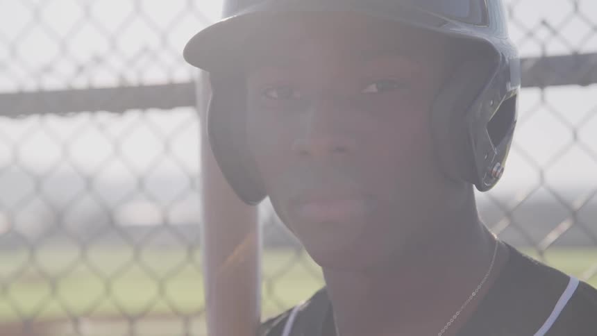 A baseball player holds his bat standing next to the field fence