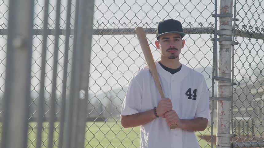 A teenage boy standing in front of a fence holding a baseball bat