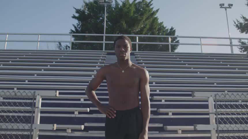 A teenage boy standing at the bottom of bleachers in a stadium