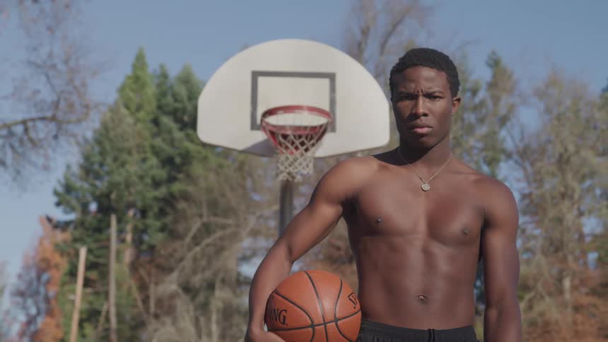 Young man on basketball court at park holding ball shirtless