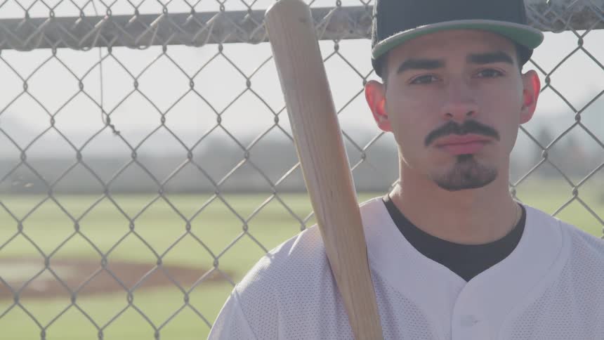 A baseball player holds his bat and stands next to the field fence