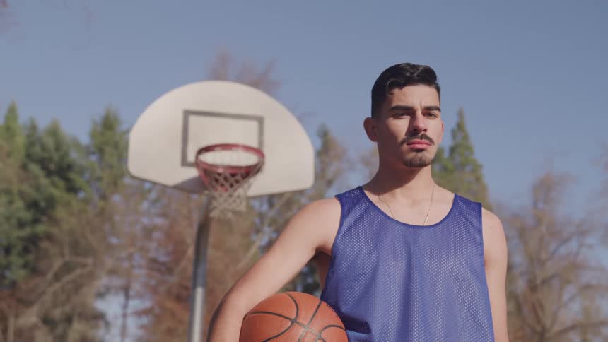 Man stands near basketball hoop holding basketball under clear blue sky