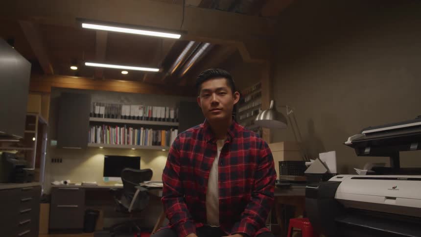 A young man in a red flannel shirt sits in an office