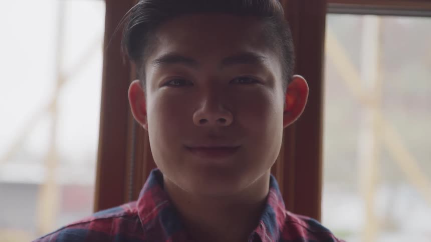 Asian boy with a plaid shirt looks at the camera smilingly on a train