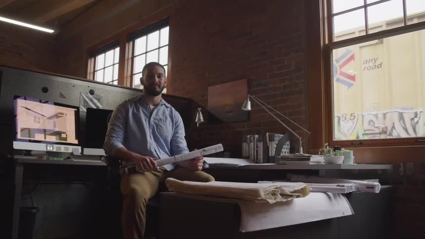 A man in an office sitting on a chair with a train moving outside the window