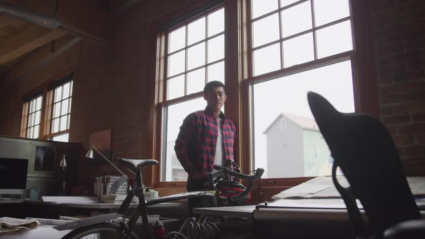 Young man with a bicycle stands near a window inside an office