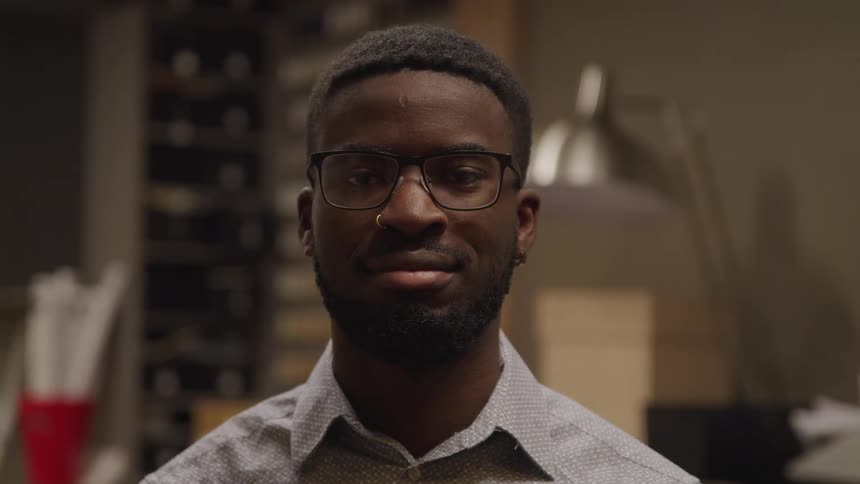 A young black man wearing glasses poses within an office
