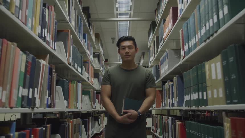 Man stands in library between bookshelves holding a book