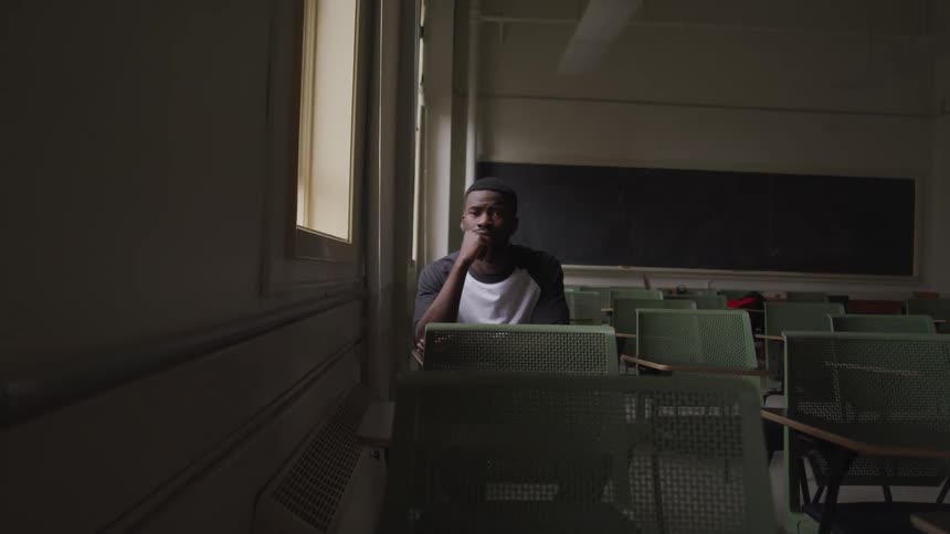 A man sits in a dark classroom by himself