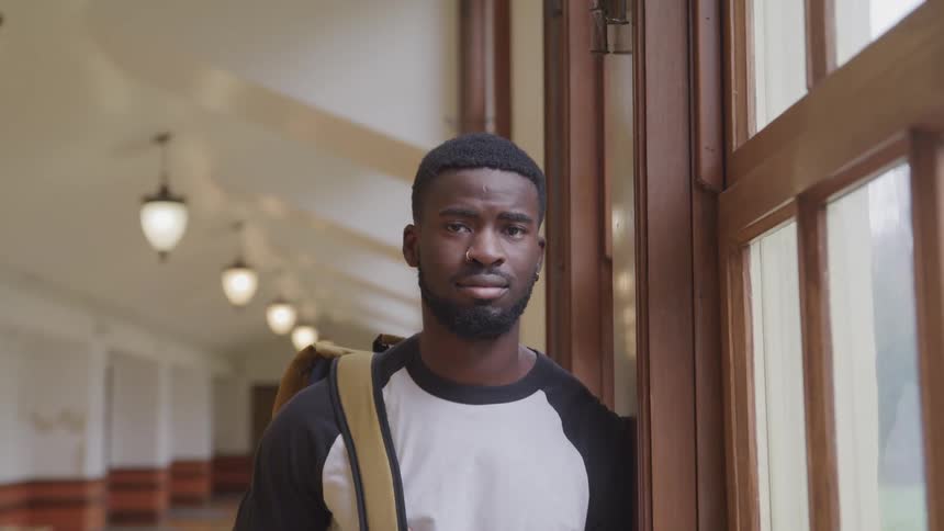 A college student poses in a hallway next to a large window