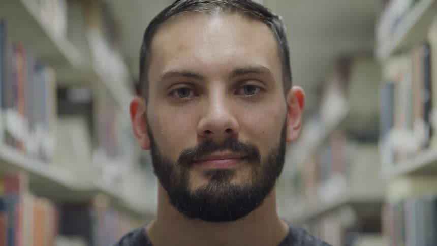 Man with a beard faces the camera with eye contact in a library