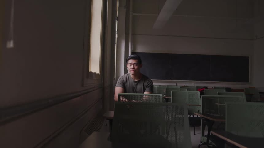 A man sits in a dark classroom by himself