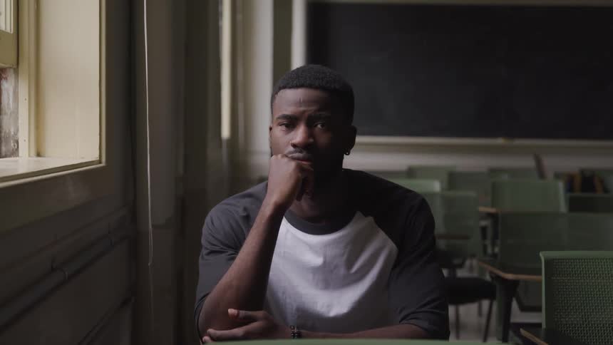 A teenage boy sits in a desk in a classroom