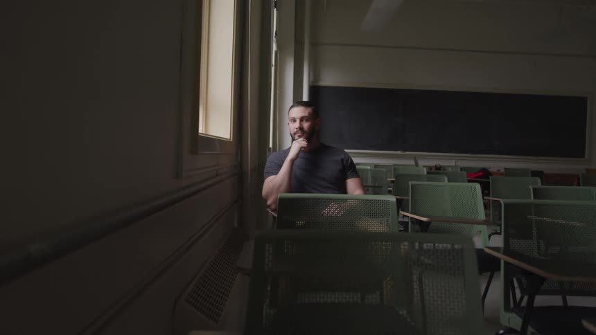 A man sits at a desk in dark empty classroom
