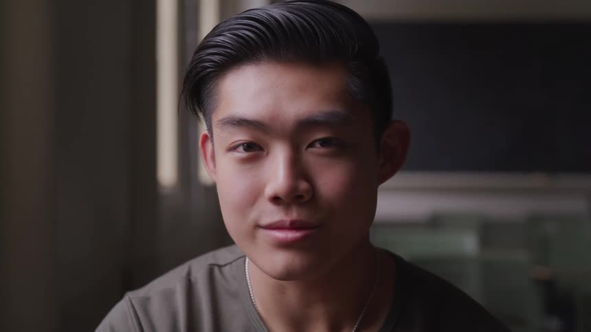 Asian man sitting in a chair faces the camera with eye contact in a classroom