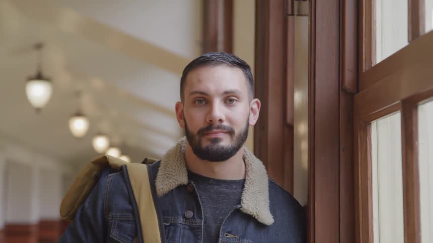Man carrying backpack leans against window sill in wide corridor