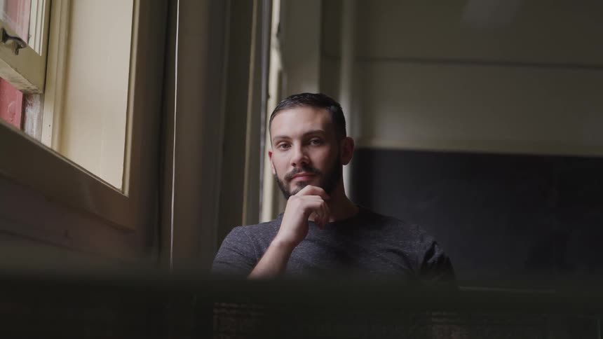 Man sitting near open window in classroom with chalkboard behind him turns to look forward