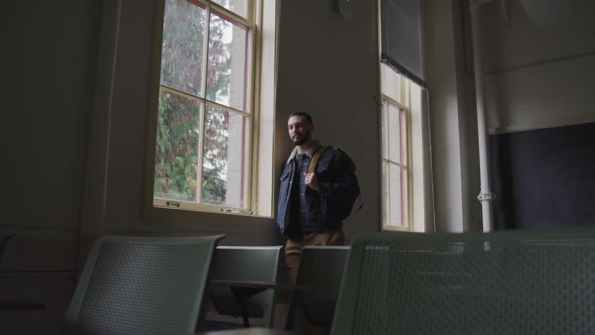 College student in empty classroom looks out window