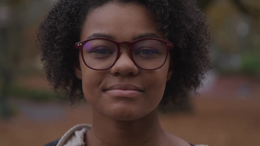 Black woman with curly hair and glasses looks at the camera smilingly