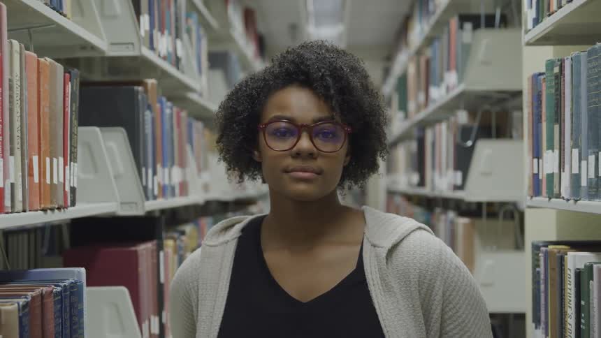 Young woman wearing glasses looks at the camera while standing in the university library