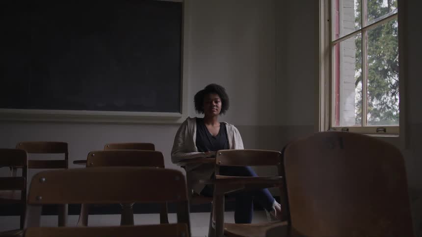 A woman sits in a dark classroom by herself