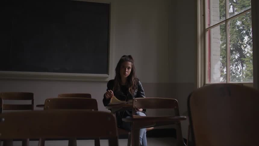 Young woman sits at desk in empty classroom
