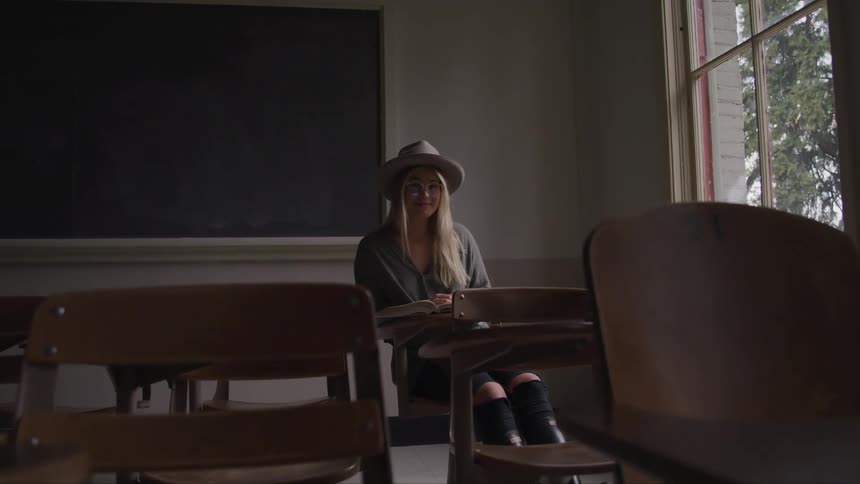 Young woman sitting in empty classroom in front of blackboard