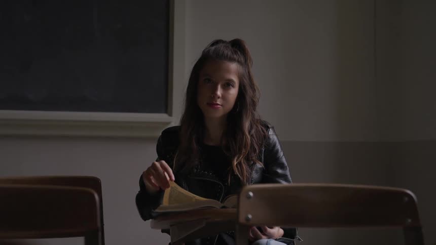 Young girl wearing black leather jacket reads a book on a desk in a classroom