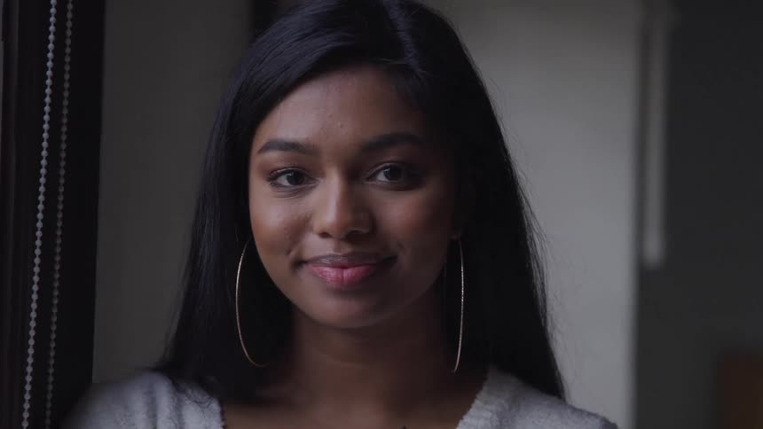 Black woman with long black hair and hoop earrings looks at the camera
