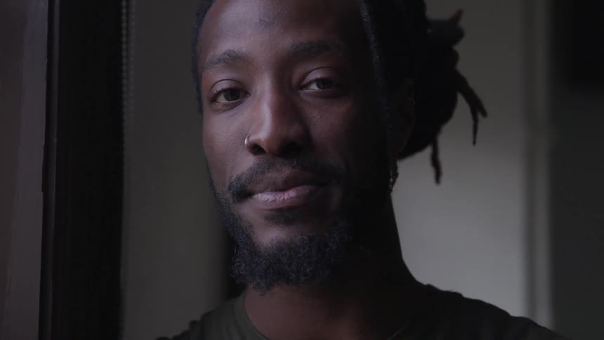 Black man with dreadlocks and beard turns to camera and smiles
