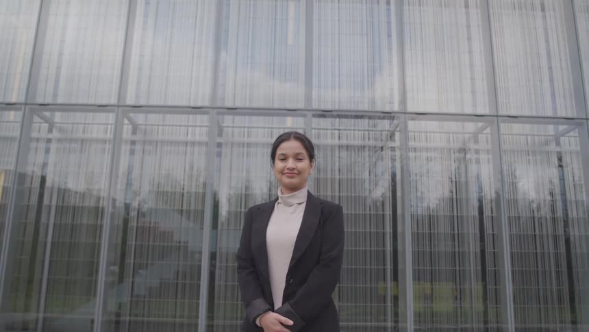 A woman is standing outdoors by a building in a city