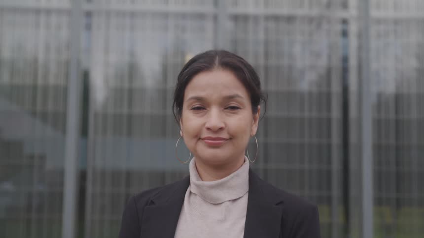 Middle aged woman with a turtleneck sweater a black blazer and hoop earrings faces the camera with eye contact