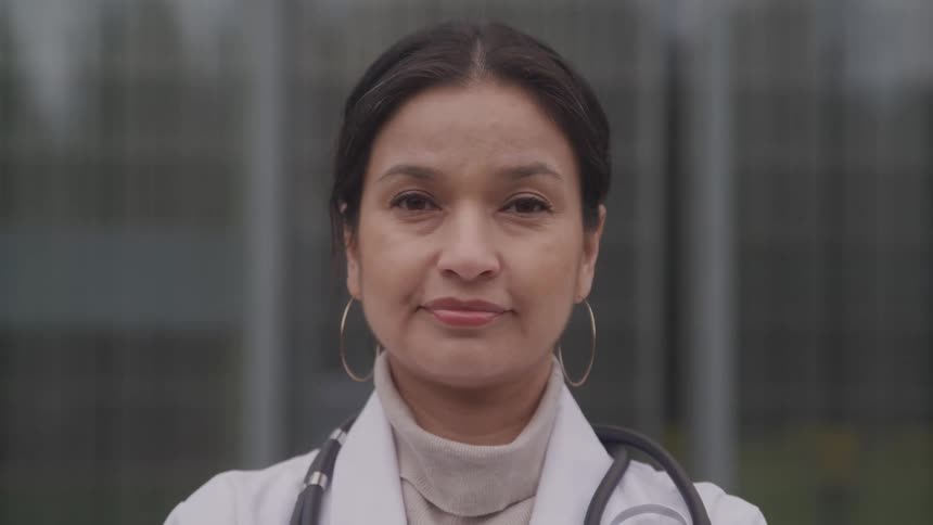 A middle aged female physician poses outdoors with her stethoscope around her neck