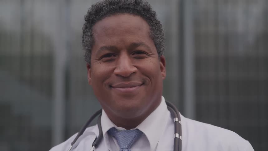 A doctor is standing outdoors and smiling