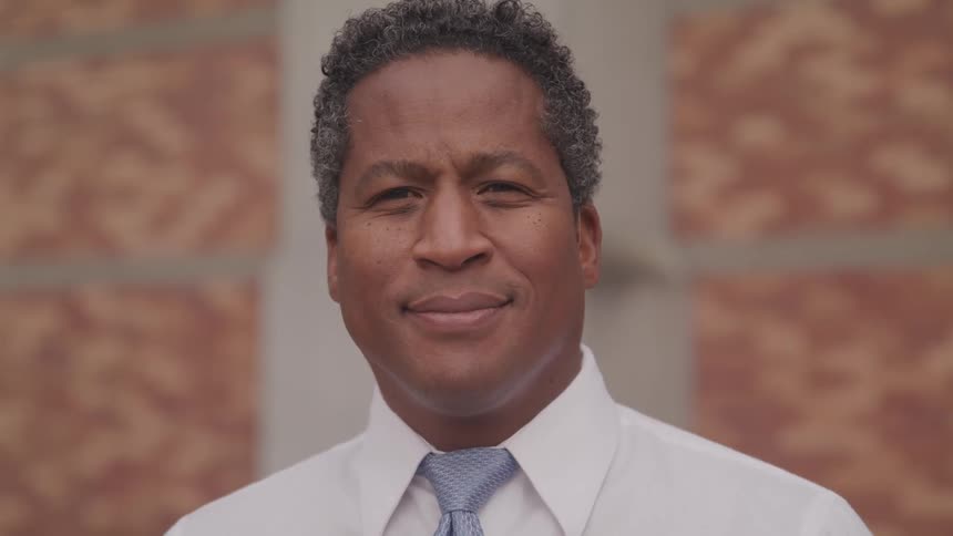 A man in a dress shirt and tie standing in an office smiling