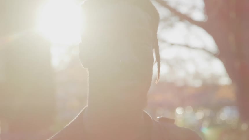 A man stands outside in a black leather jacket on a fall day