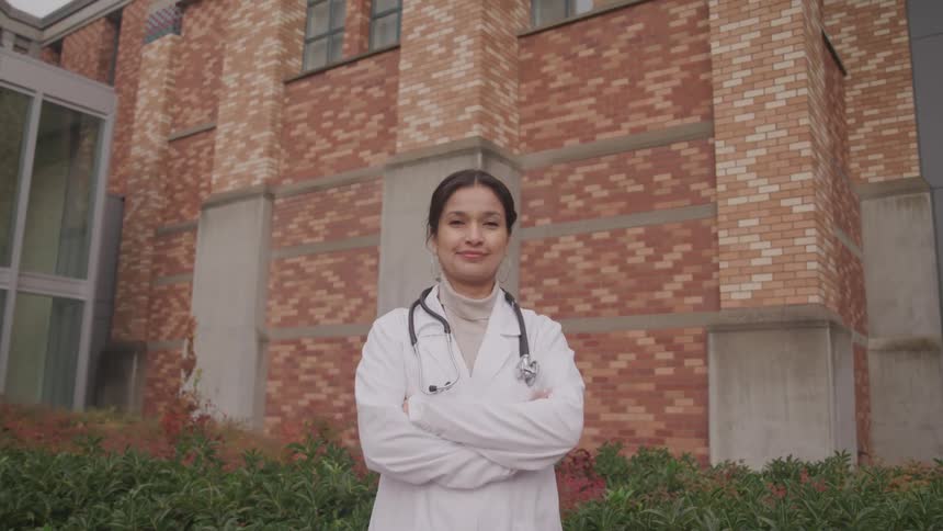 Woman in lab coat with stethoscope outside of brick building