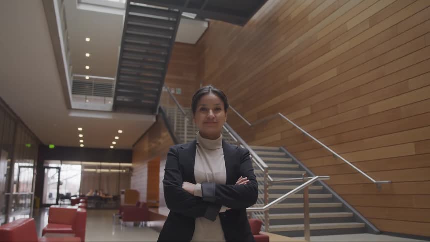 A woman stands with her arms crossed in front of a staircase on the first floor of an office building