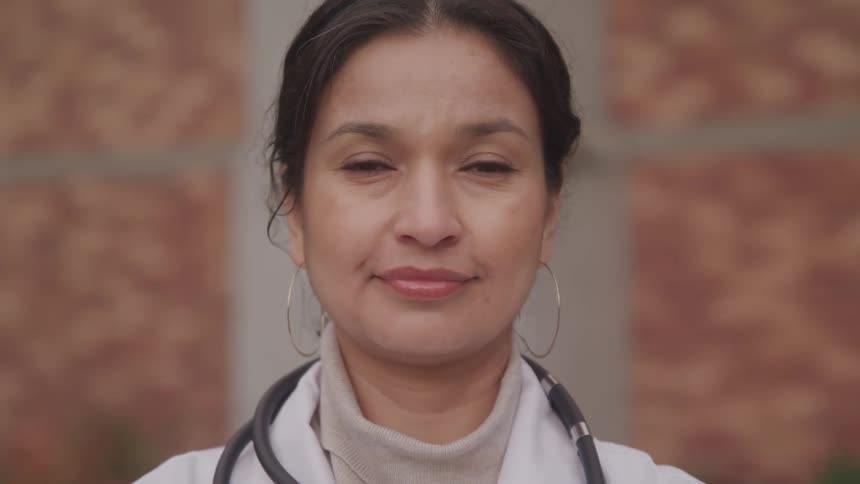 Woman in lab coat with stethoscope in front of brick wall
