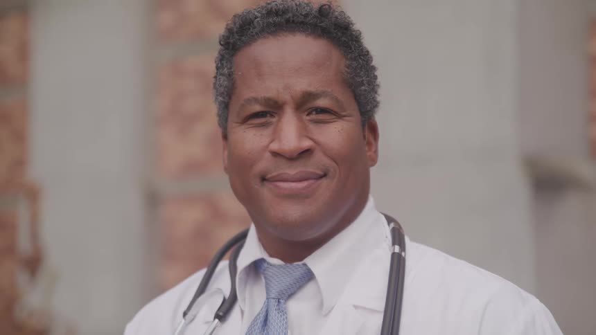 An african american physician poses with a smile on his face and a stethoscope around his neck