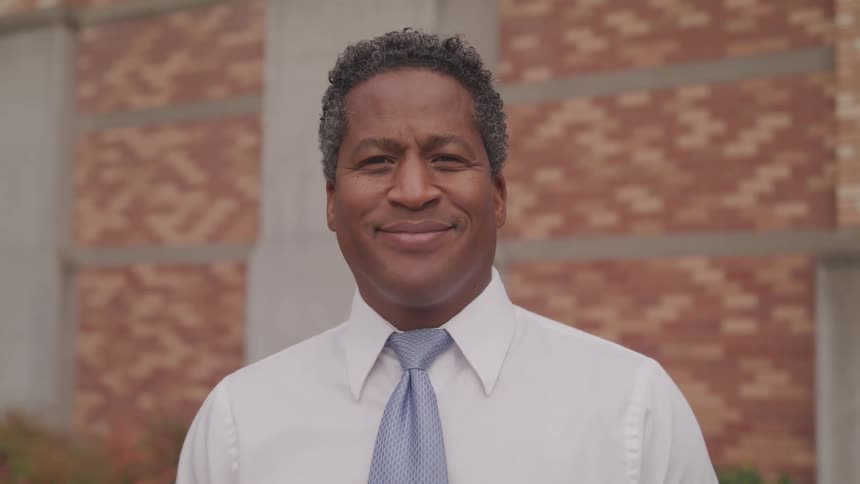 Man wearing a shirt and a tie looks at the camera outside a building