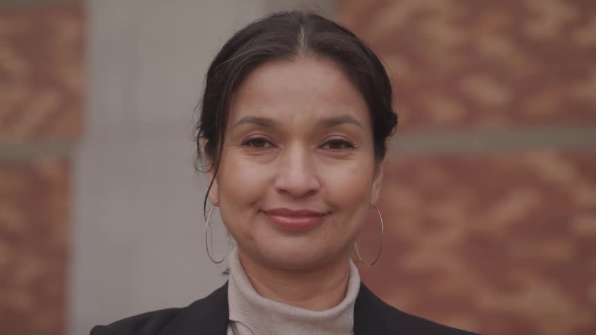 A hispanic woman with hoop earrings and a turtle neck is looking ahead and smiling