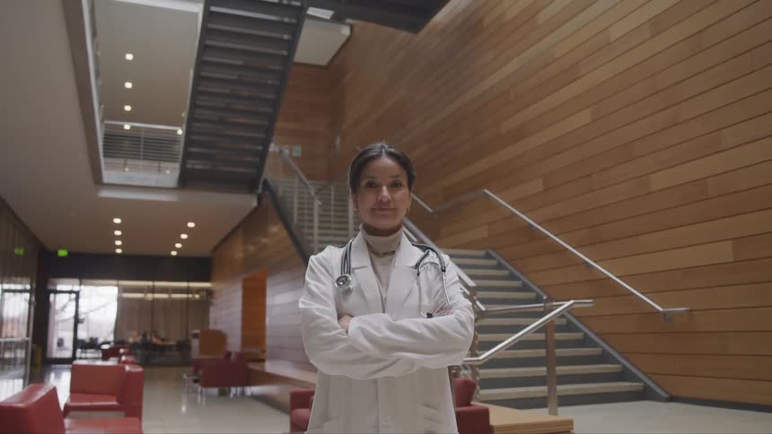 A woman wearing a doctor lab coat stands in the lobby of a large building
