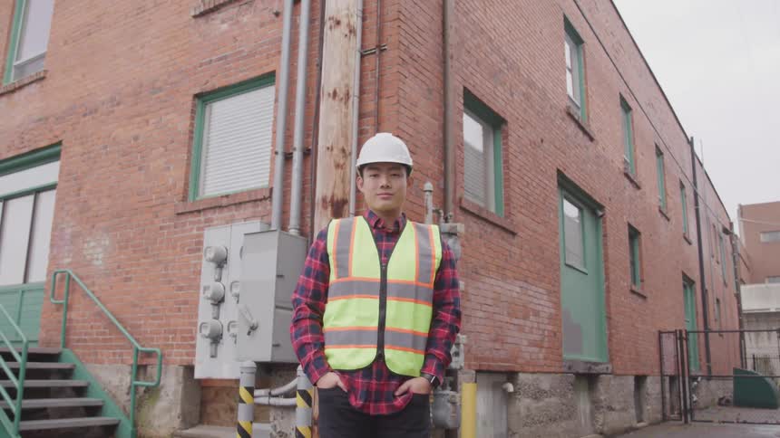 A man wearing a construction vest and hard hat stands outside of a city building