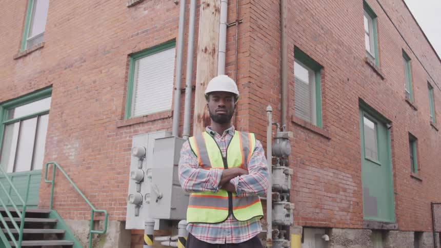 A man standing with a hard hat and a vest with a building in the background