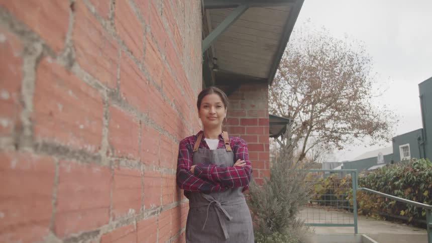 A hispanic woman in an apron looks into the camera as she looks into the camera