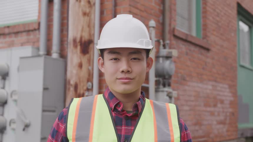 Young man in hard hat and vest smiles slightly