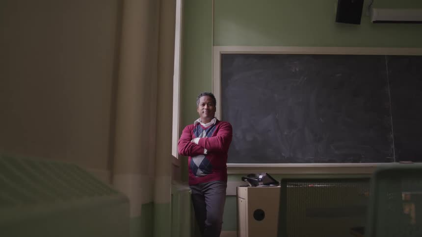 A man stands in an empty classroom next to a window